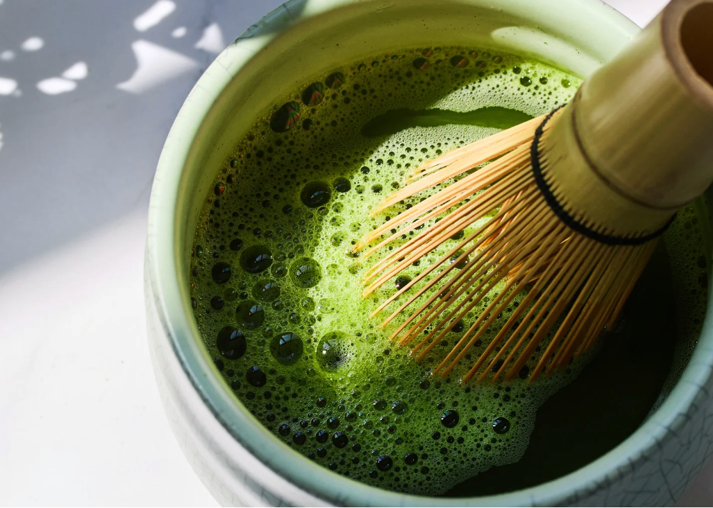 Matcha green tea being whisked in a white bowl with a wooden whisk.