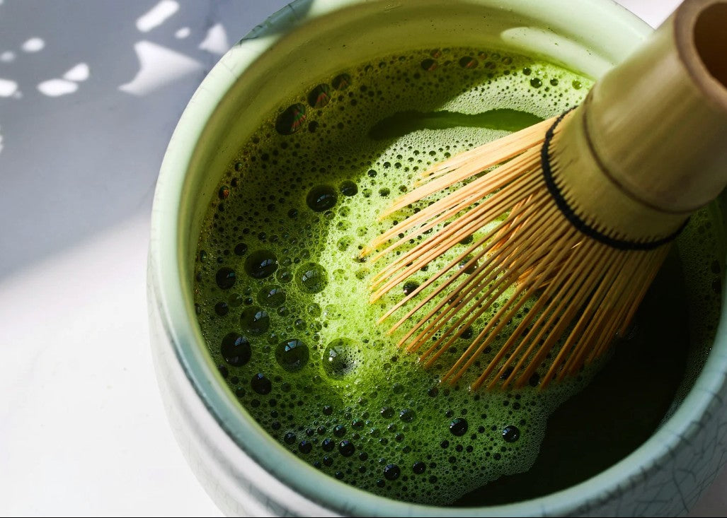 Matcha green tea being whisked in a white bowl with a wooden whisk.